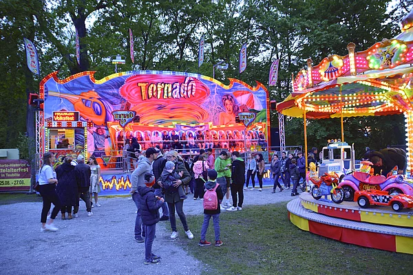 Grell bunt beleuchtete Fahrgeschäfte und ein Karussell vor der Schlossruine.