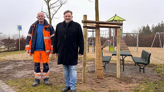 Vor dem neu aufgestellten Sitzbereich am Spielplatz Steinbruchäcker stehen ein Mitarbeiter des Bauhofs und der Erste Bürgermeister gemeinsam für ein Foto.