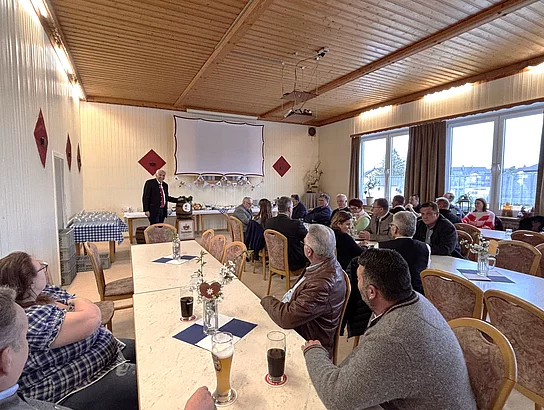 Besucherinnen und Besucher sitzen an Tischen in einem Saal und verfolgen eine Ansprache im Rahmen der Bierprobe.