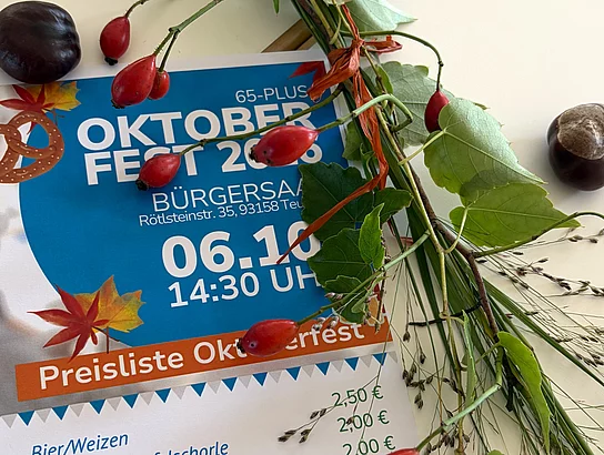 Ein Veranstaltungsplakat zum Oktoberfest liegt auf einem Tisch und ist mit Hagebuttenzweigen, grünen Blättern und Kastanien herbstlich dekoriert.