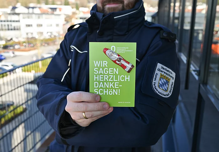 Auf dem Bild hält eine uniformierte Person eine grüne Karte mit der Aufschrift „Wir sagen herzlich Dankeschön!“ sowie einem kleinen Schoko-Nikolaus darauf gut sichtbar in die Kamera.