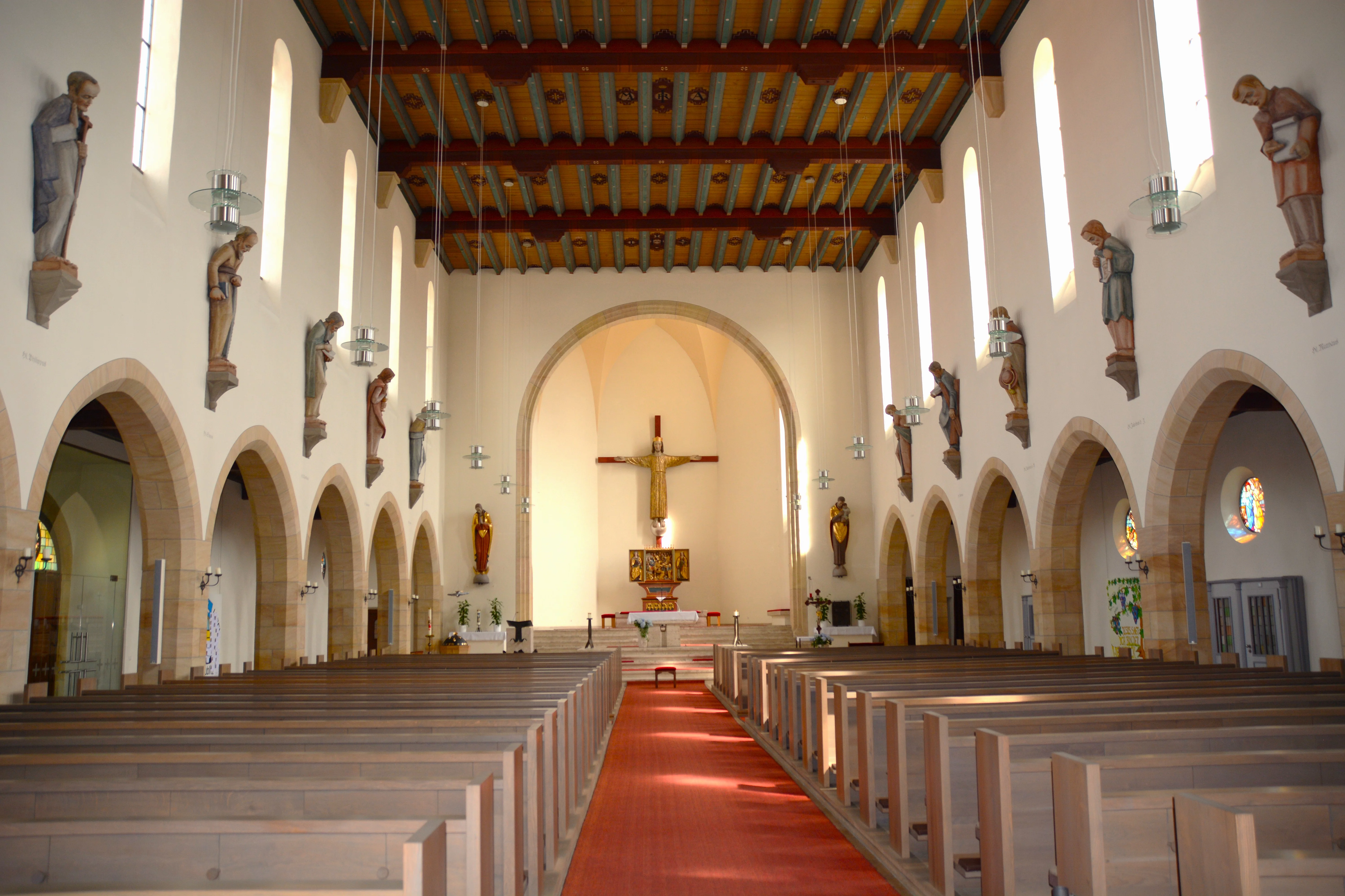 Imposanter hallenähnlicher Innenraum einer Kirche. In der Mitte des Bildes Jesus am Kreuz.