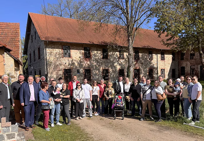 Eine große Gruppe von Menschen steht bei sonnigem Wetter vor einem historischen Gebäude und posiert gemeinsam für ein Foto.