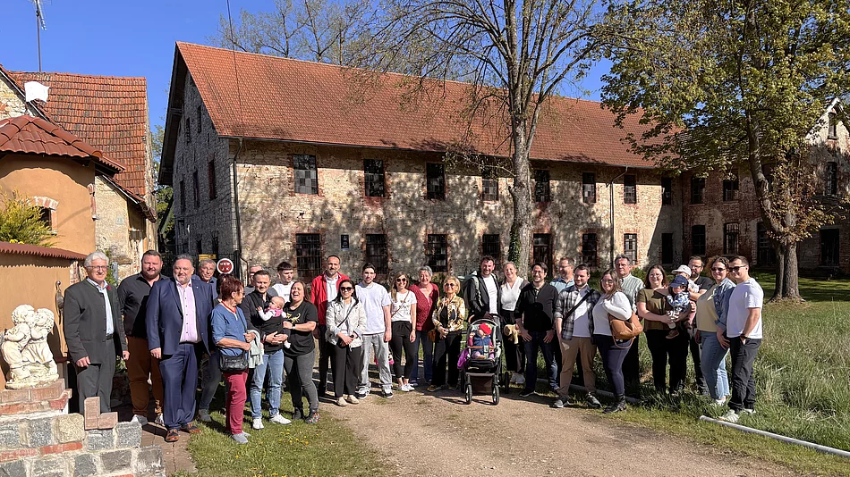 Eine große Gruppe von Menschen steht bei sonnigem Wetter vor einem historischen Gebäude und posiert gemeinsam für ein Foto.