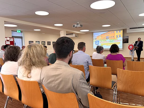 Die Gäste sitzen im Saal des Mehrgenerationenhauses und verfolgen das Grußwort von Bürgermeister Thomas Beer am Rednerpult.