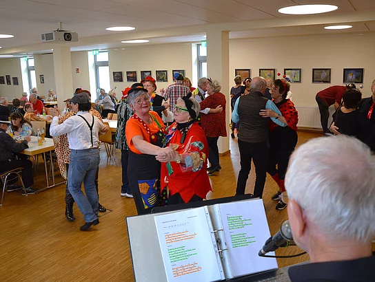 Aus der Perspektive eines Musikers sieht man viele tanzende Paare im Raum, während im Vordergrund ein Mikrofon und Notenblätter zu erkennen sind.