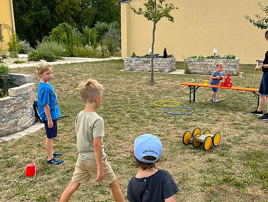 Mehrere Kinder spielen im Garten des Mehrgenerationenhauses an einer Mitmachstation und versuchen, mit Wurfspielen Dosen zu treffen.
