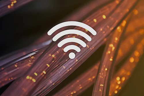 Ein weißes WLAN-Symbol ist vor einem abstrakten Hintergrund mit leuchtenden Glasfasersträngen in Orange- und Violetttönen dargestellt.