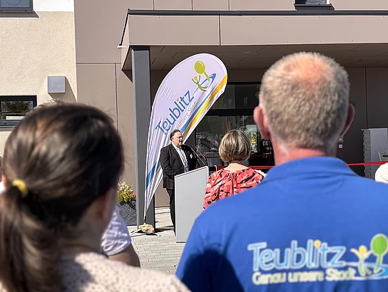 Ein Redner spricht zur Eröffnung, während die Besucher aufmerksam zuhören.