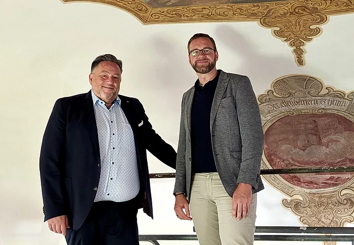 Bürgermeister Thomas Beer und Pfarrer Lucas Lobmeier stehen auf dem Arbeitsgerüst unmittelbar unter einem restaurierten Deckengemälde der Marien-Wallfahrtskirche Saltendorf. Im Hintergrund ist ein weiteres historisches Wandmotiv zu sehen.