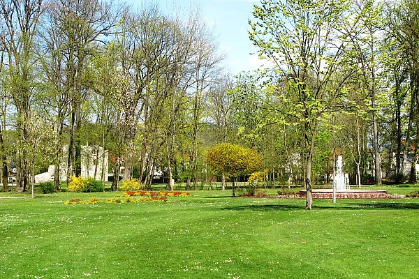 Blick über die Liegewiese im Frühling mit Springbrunnen und Ruine im Hintergrund.