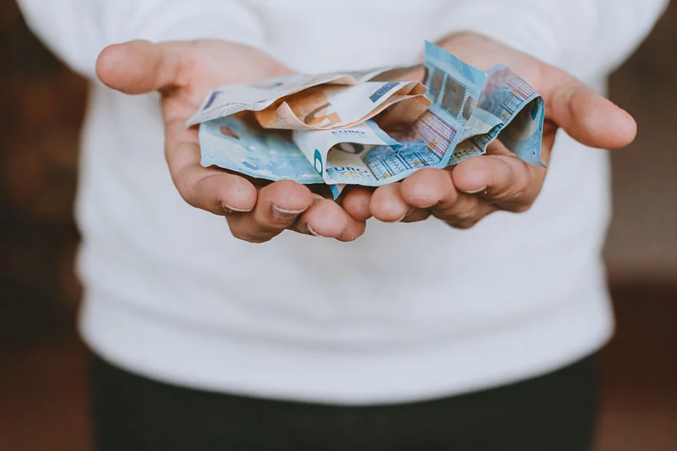 Aufgeschlagene Hände eines Mannes auf dem Bargeld liegt, das symbolisch gereicht werden.