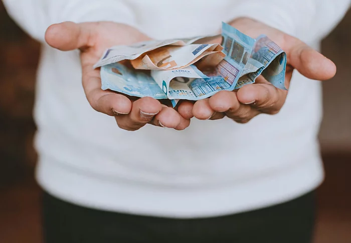 Aufgeschlagene Hände eines Mannes auf dem Bargeld liegt, das symbolisch gereicht werden.