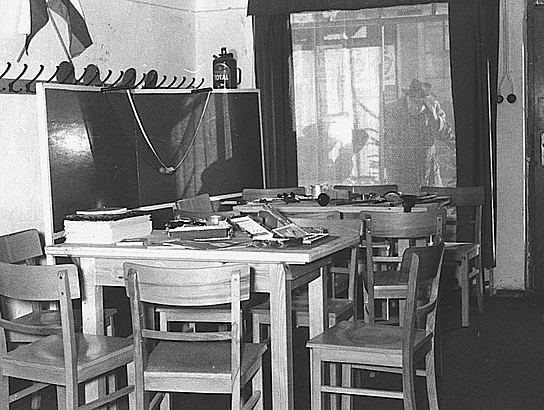 Eine weitere historische Schwarz-Weiß-Aufnahme zeigt den Innenraum des Jugendheims aus einer anderen Perspektive. Mehrere Tische und Stühle stehen im Raum, an den Wänden befinden sich Garderobenhaken. Durch das Fenster fällt Tageslicht in den Aufenthaltsbereich.