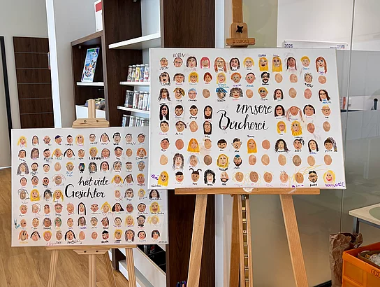 Zwei Leinwände zeigen viele gemalte Gesichter von Kindern und Erwachsenen in der Bücherei.