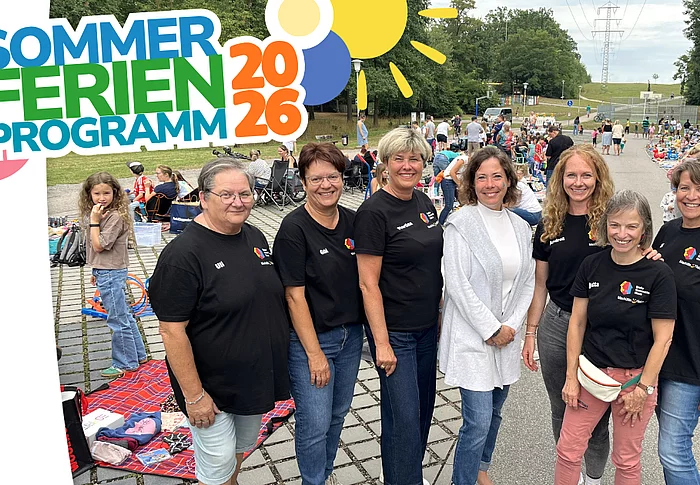 Gruppenfoto von sieben Frauen vor dem gut besuchten Kinderwarenflohmarkt in Maxhütte-Haidhof. Im Hintergrund bieten zahlreiche Kinder und Familien auf Decken und an Ständen Spielsachen, Kleidung und weitere Kinderartikel zum Verkauf an. Die Grafik trägt links oben den Schriftzug „Sommerferienprogramm 2026“.