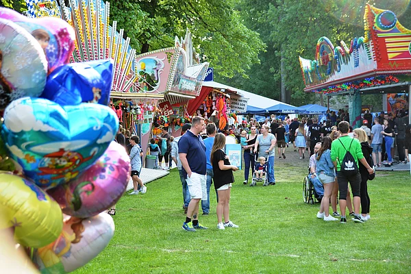 Blick in den Festplatz mit vielen Besuchern. Im Vordergrund ein Bündel aufgeblasener Heliumluftballons.