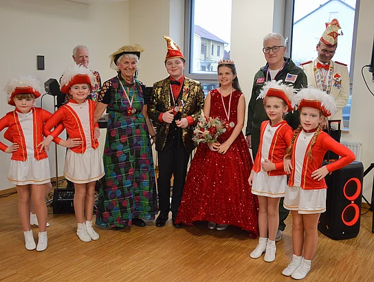 Kinder und Erwachsene stehen gemeinsam für ein Erinnerungsfoto, wobei die Kinder festliche rote Tanzkostüme tragen und die Erwachsenen ebenfalls verkleidet sind.