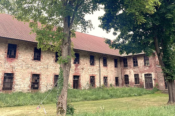 Ein sehr altes Gebäude aus Steinen erbaut, umgeben von saftig grünen Wiesen und Bäumen.