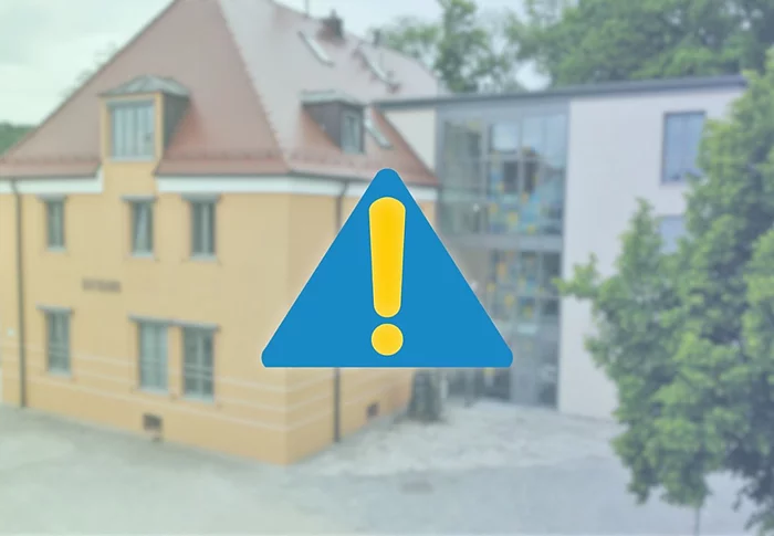 Auf einer gelblich verblassten Hintergrundaufnahme des Rathauses steht mittig ein großes, dunkelblaues Warnsymbol mit Ausrufezeichen.