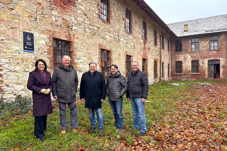Vor der verwitterten Steinfassade des alten Schleifgebäudes steht eine Gruppe von fünf Personen für ein Foto, umgeben von herbstlichem Laub.