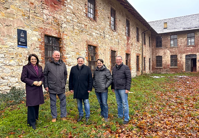 Vor der verwitterten Steinfassade des alten Schleifgebäudes steht eine Gruppe von fünf Personen für ein Foto, umgeben von herbstlichem Laub.