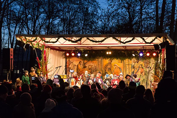 Gäste lauschen gebannt den singenden Kindern auf der hell erleuchteten Bühne.