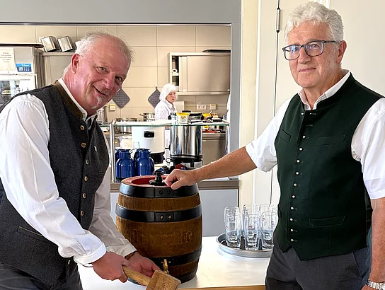 Georg Fleischmann und Robert Wutz stehen mit Holzschlegeln neben einem Bierfass und übernehmen gemeinsam den Fassanstich beim Senioren-Oktoberfest im Mehrgenerationenhaus.