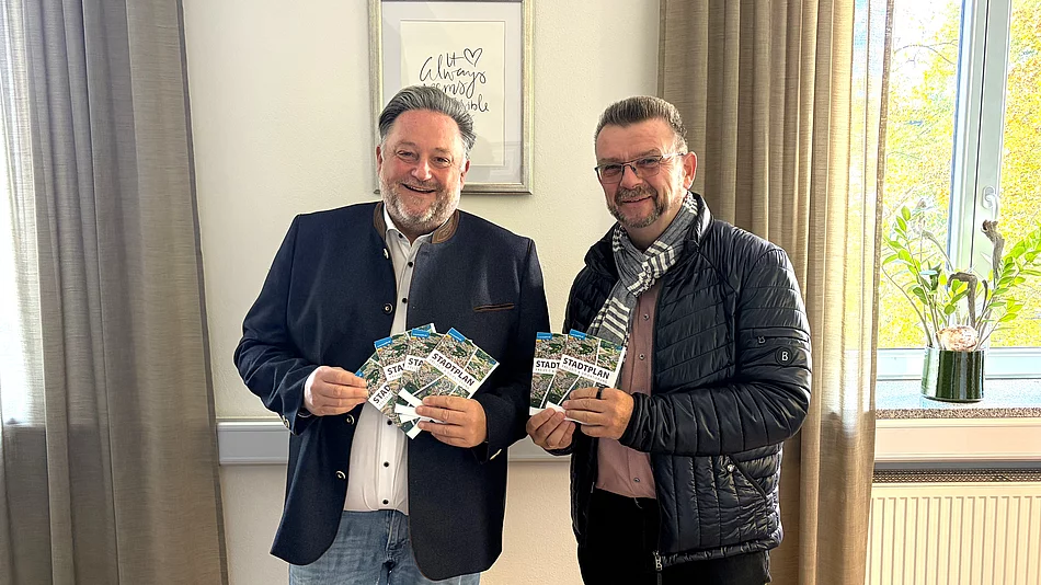 Zwei Männer stehen nebeneinander in einem Büro und präsentieren gemeinsam mehrere Exemplare des neuen Teublitzer Ortsplans.