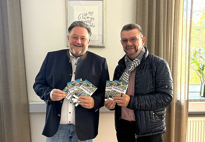 Zwei Männer stehen nebeneinander in einem Büro und präsentieren gemeinsam mehrere Exemplare des neuen Teublitzer Ortsplans.