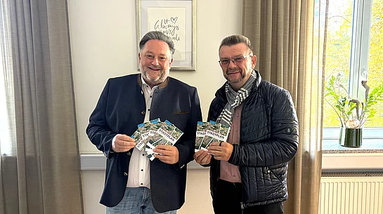 Zwei Männer stehen nebeneinander in einem Büro und präsentieren gemeinsam mehrere Exemplare des neuen Teublitzer Ortsplans.