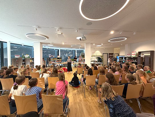 Zahlreiche Kinder sitzen auf Stühlen in der neuen Stadtbücherei und verfolgen gemeinsam die Preisverleihung des Sommerferien-Leseclubs.