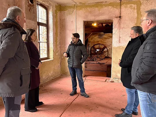 In einem stark gealterten Raum mit bröckelndem Putz und Blick auf historische Maschinen erläutert ein Mann einer kleinen Besuchergruppe die Bedeutung des Gebäudes.