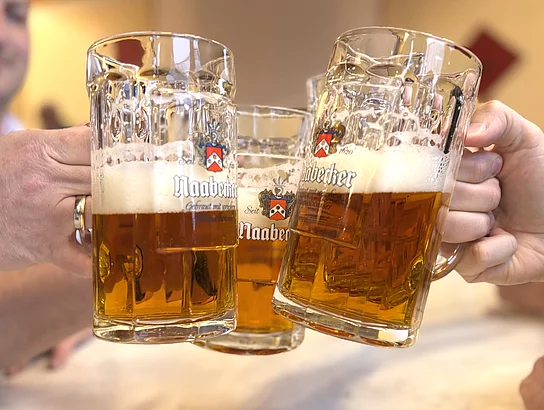 Mehrere Bierkrüge mit frisch gezapftem Bier werden zum Anstoßen zusammengeführt.