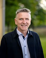 Ein Mann mit kurzem Haar und Hemd schaut freundlich und aufmerksam.
