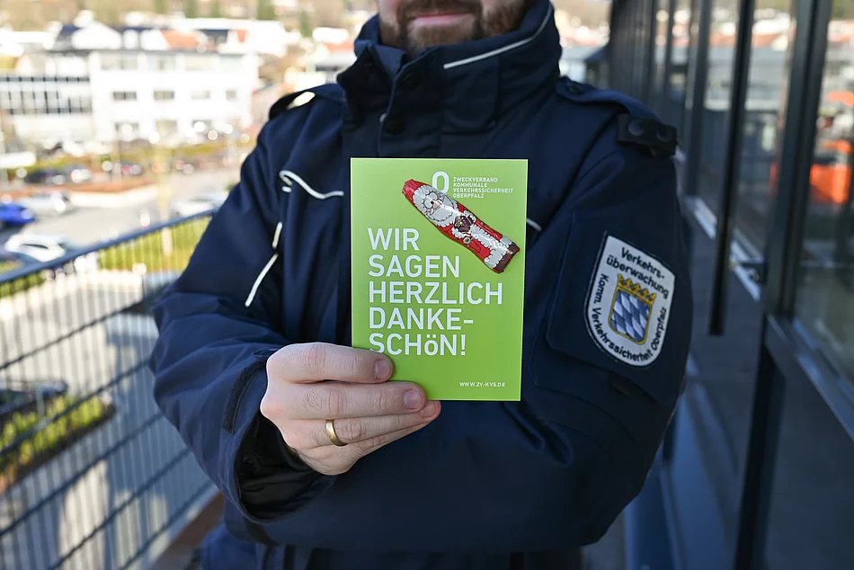 Auf dem Bild hält eine uniformierte Person eine grüne Karte mit der Aufschrift „Wir sagen herzlich Dankeschön!“ sowie einem kleinen Schoko-Nikolaus darauf gut sichtbar in die Kamera.
