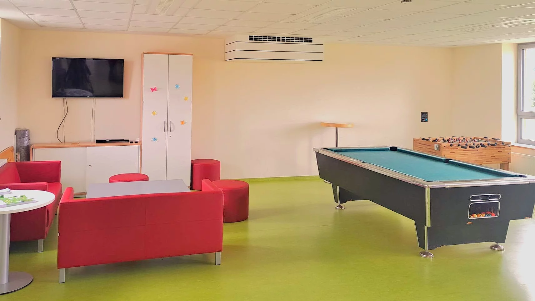 Blick in den Jugendtreff mit einer roten Couch als Sitzecke, Billardtisch und Tischkicker.