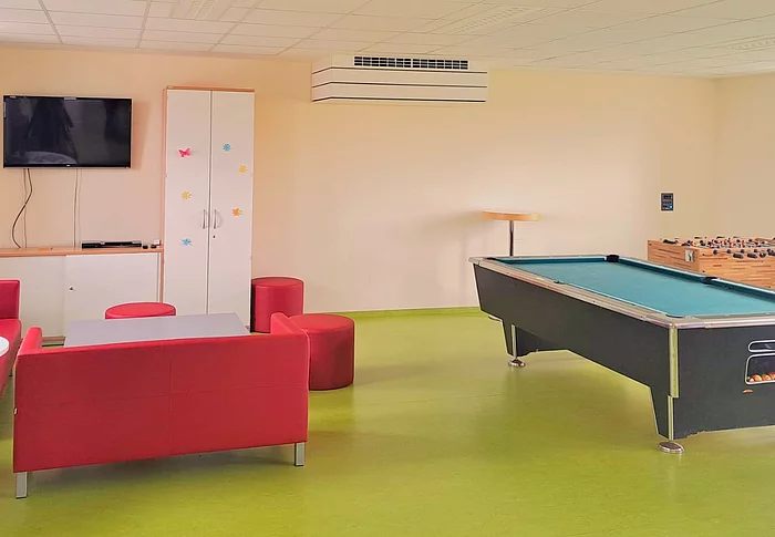 Blick in den Jugendtreff mit einer roten Couch als Sitzecke, Billardtisch und Tischkicker.